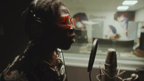 Black Singer in Headphones Recording Vocals in Soundproof Studio Booth