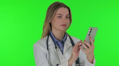 Portrait of Female Doctor Browsing phone on green background