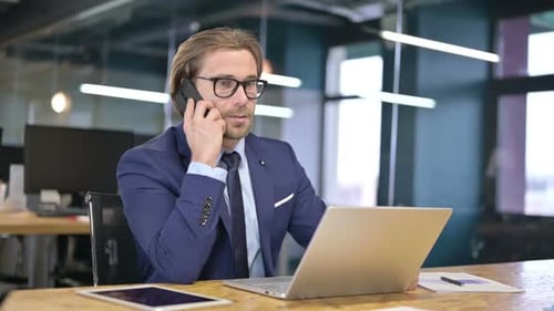 Man in Suit Answers Phone at Office Desk