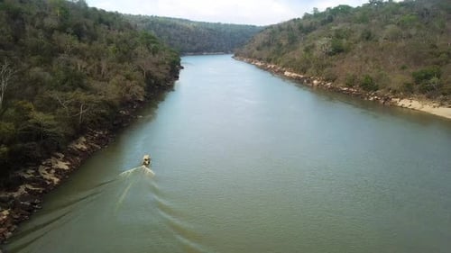 4k video drone footage of a single boat going down a river surrounded by trees on a wildlife reserve