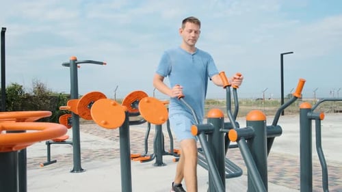 Young Male Doing Cardio Workout Exercises on Elliptical Trainer in a Street Gym Active Man