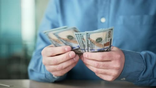 Close up. Male hands count one hundred dollar US bills. Mature businessman in blue shirt counting