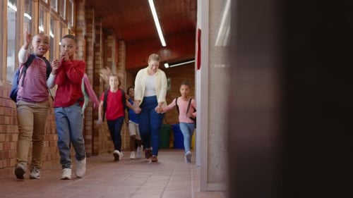 Walking in school hallway, female teacher and diverse group of children holding hands