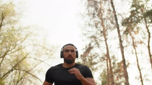 Young Muscular Athlete in Headphones Running with a Focused Face in an Alley in a City Park Concept