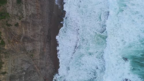 Ocean huge turquoise waves crashing at sunset on sand beach surrounded by cliffs. Aerial top shot.