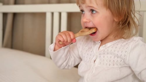 Child Chews Wooden Toy in White Bed