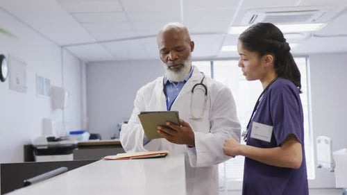 Diverse male and female doctors using tablet and talking at hospital