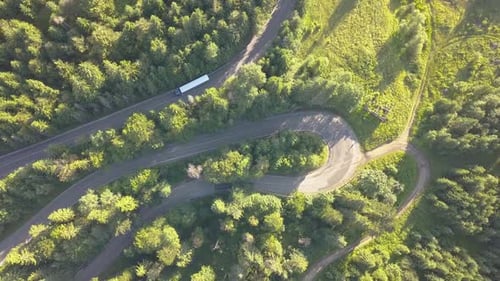 Aerial View of Winding Road with Mowing Cars and Trucks in High Mountain Pass Trough Dense Woods