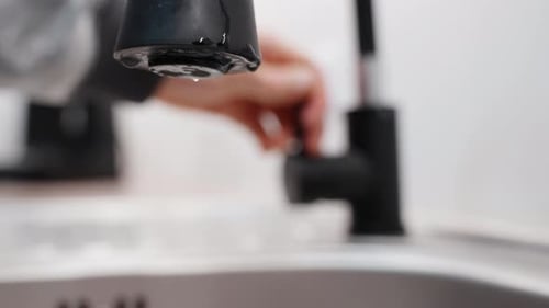 Water Dripping from Black Faucet in a Home