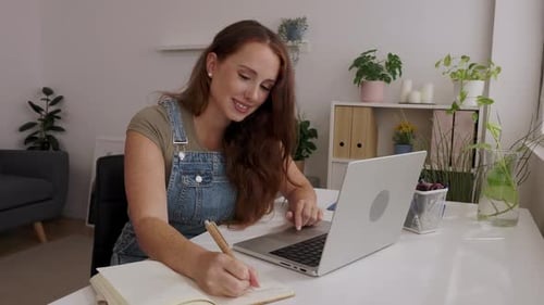 Woman Writing and Using Laptop at Desk Indoors