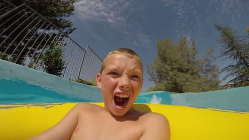 Excited boy enjoys water park ride in summer