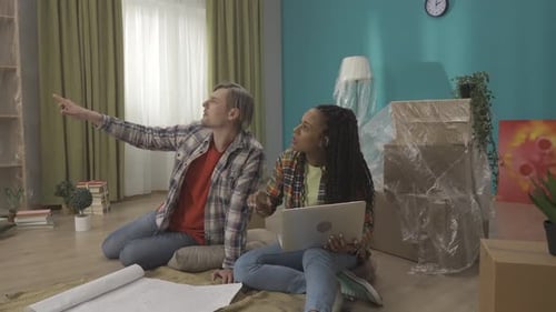 A Couple Sits on the Floor Surrounded By Unpacked Cardboard Boxes in the Living Room A Couple is