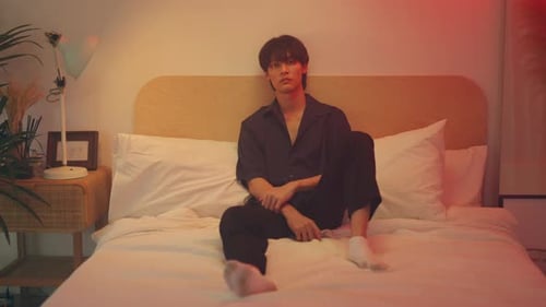 Young Adult Sits on Bed in Moody Lit Room