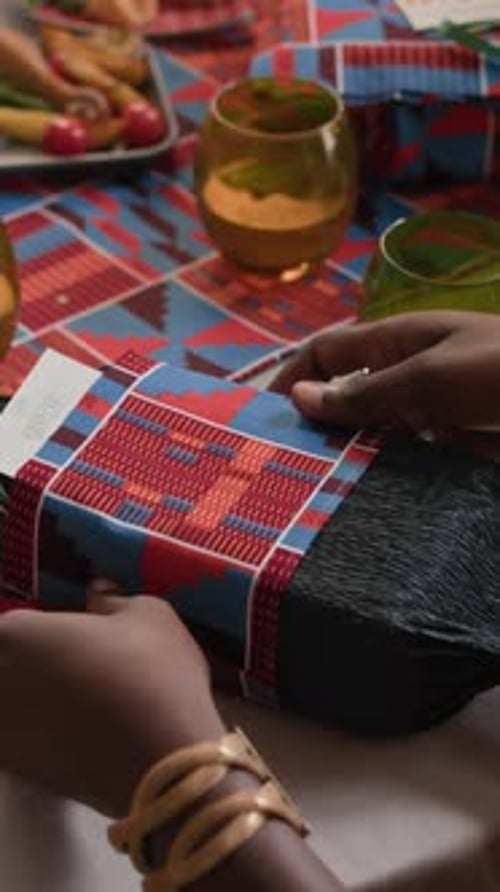 Vertical of Black Woman Unwrapping Gift at Festive Dinner Table