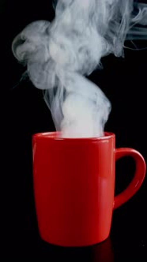 White swirling steamy smoke or smog from red cup coffee or tea on black background.