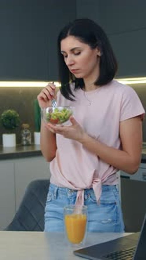 Woman in Kitchen Eating Salad and Drinking Juice