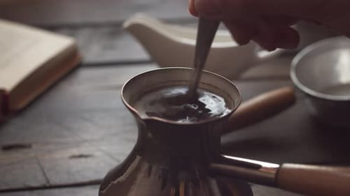 Stirring Hot Coffee with Spoon in Cezve on Wooden Table