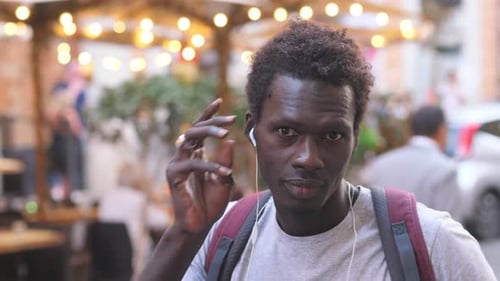 young african man on the street puts on headphones and smiles at the camera