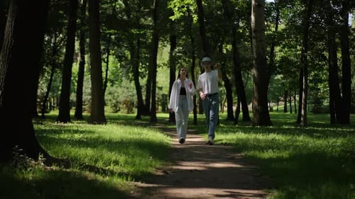 Ein Mann mit Sonnenhut und ein Mädchen mit langen Haaren gehen einen Feldweg im Wald entlang und reden