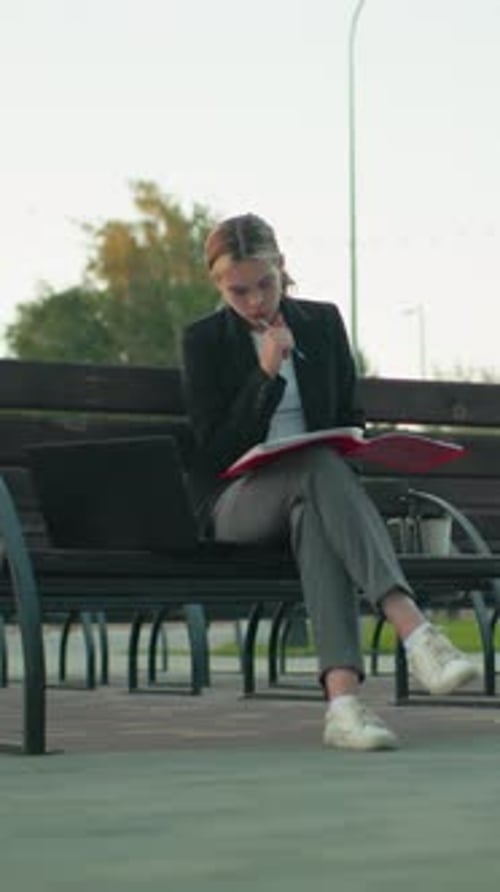 Focused Student Reading Book on Urban Bench with Laptop and Coffee in Quiet Park
