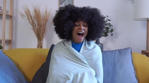 Afroamerikanerin gähnt, während sie zu Hause auf dem Sofa sitzt