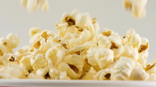 Popcornkörner fallen isoliert auf weißem Hintergrund in einen rot-weiß gestreiften Eimer.