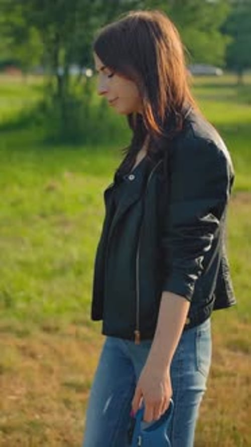 Vertical of A Young Female in Jeans Leading Her Dog for a Walk in the Park on a Leash