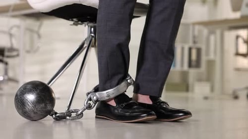 Businessman with metal ball and chain on his leg in office, closeup