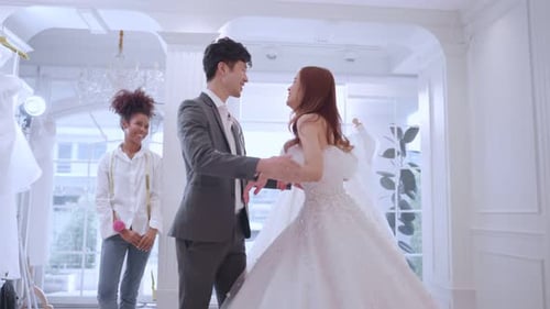 Asian beautiful bride trying on wedding gown with her fiance in studio.