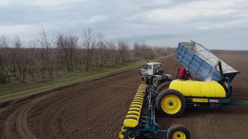 Blue tractor with yellow seeder working on the field in Ukraine OA