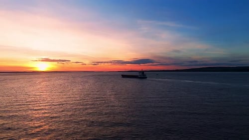 Amid the golden hour's glow, an aerial drone reveals a peaceful barge sailing beneath Humber Bridge