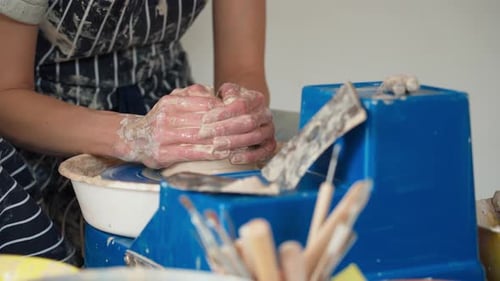 A female potter works on a potter's wheel, making a ceramic pot from clay in a pottery workshop.