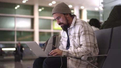Traveler Male Using Laptop in Airport Terminal Typing Concentrated
