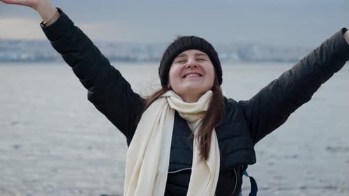 Cheerful young woman with a backpack standing on a cliff at the sea coast