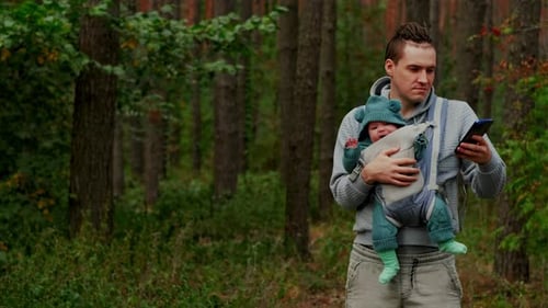 Father and Newborn Baby in a Sling in the Autumn Forest Man with Mobile Phone Happy Family