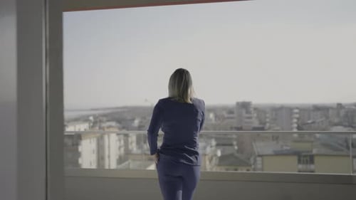 Woman Talks on the Phone Going Out Onto the Balcony of the Apartment