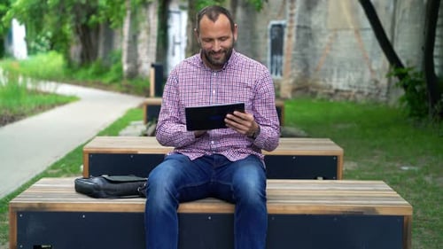 Young man browsing the internet on tablet in city park on sunny day