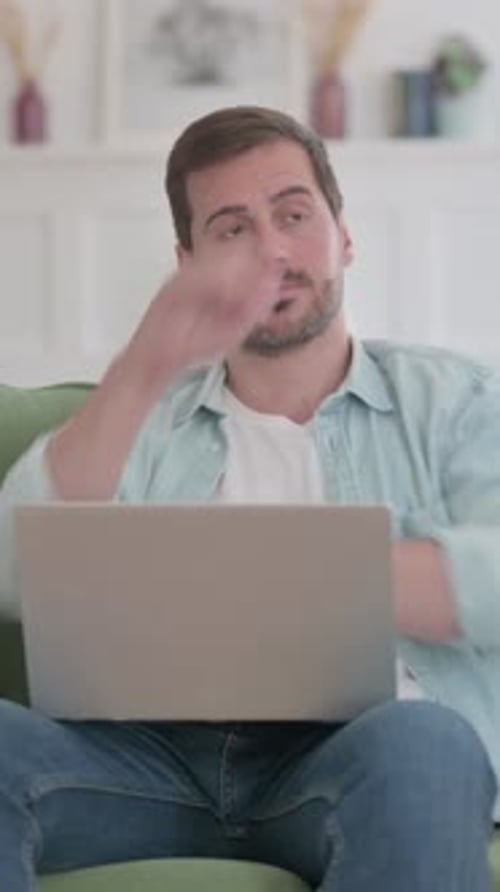 Young Man Thinking while Working on Laptop on Sofa, vertical video