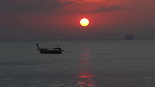 Un barco de cola larga se encuentra en el mar frente a una hermosa puesta de sol