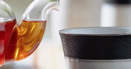 Red Tea Poured into Teacup from Glass Teapot