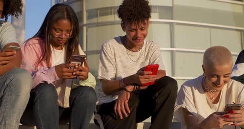Big Group of Happy Teenage Friends Each One Looking at Their Phone in a Bench in the Street