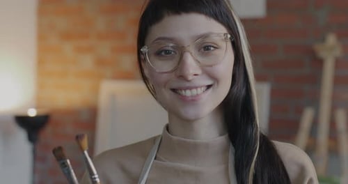 Slow Motion Portrait of Happy Young Lady Artist Standing in Loft Style Studio Holding Brushes