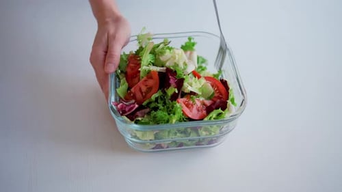 Mixing Fresh Salad with Fork in Glass Bowl