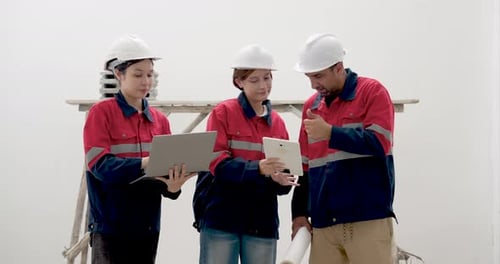 Asian female engineer checks laptop report with woman inspector and male contractor, reviewing