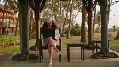 Woman Freelancer Works Online on Laptop Sits on Wooden Chair on Tropical Beach