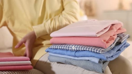 Woman with stack of clothes on sofa indoors, closeup