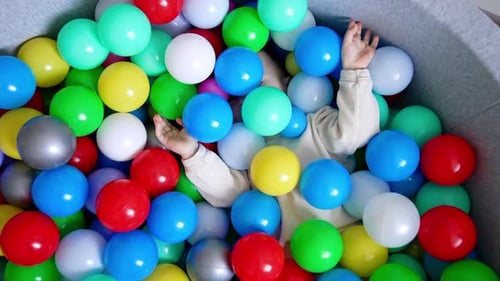 Baby boy lies hiding in the colorful balls in a dry pool.