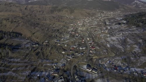 Drone view of a small farming community in the valley below a mountain range lined with pine trees a