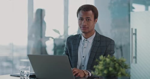 Cheerful Young African Employee Using Laptop Computer and Shrugging Shoulders to Camera Hesitation