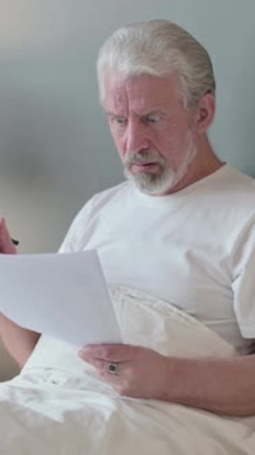 Senior Man Reading Document in Bed with Concern